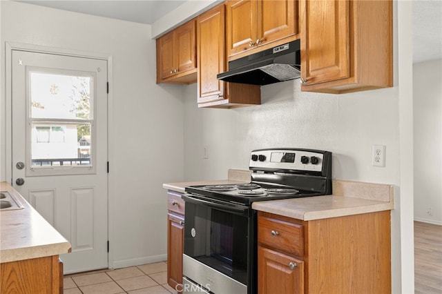 kitchen featuring electric range, brown cabinets, under cabinet range hood, light countertops, and baseboards