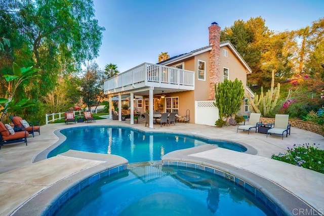 back of house with stucco siding, a patio, an outdoor pool, an in ground hot tub, and a chimney