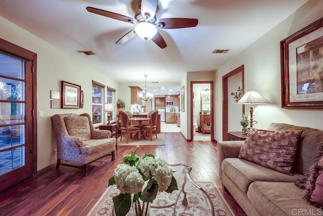 living area with dark wood finished floors, visible vents, ceiling fan with notable chandelier, and baseboards