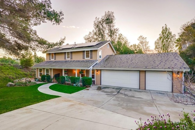 view of front of house featuring a front lawn, roof mounted solar panels, covered porch, a garage, and driveway