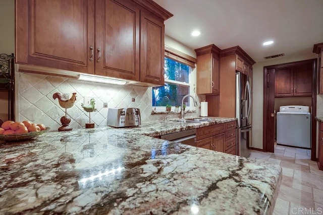 kitchen with visible vents, a sink, light stone counters, washer / clothes dryer, and stainless steel appliances