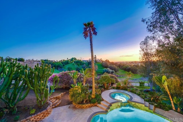 pool at dusk with an in ground hot tub and a patio