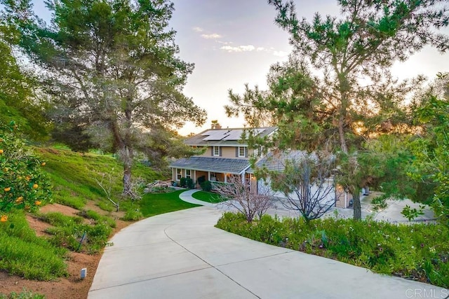 view of front of house featuring a porch, concrete driveway, a front yard, roof mounted solar panels, and a chimney