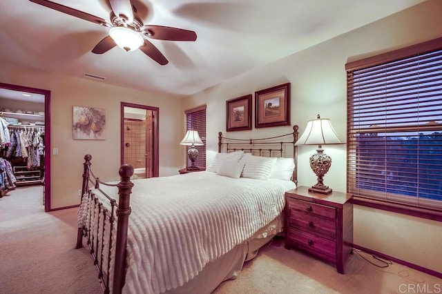 bedroom with a walk in closet, light colored carpet, visible vents, and baseboards