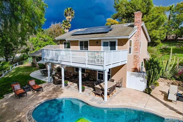 back of property with fence, a wooden deck, stucco siding, a patio area, and roof mounted solar panels