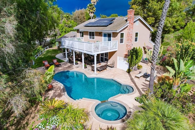 rear view of property with a patio, solar panels, an in ground hot tub, an outdoor pool, and a chimney