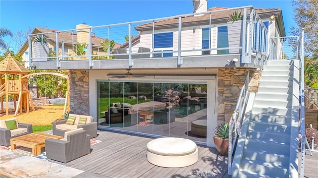 rear view of property with a balcony, a ceiling fan, stairs, stone siding, and a playground