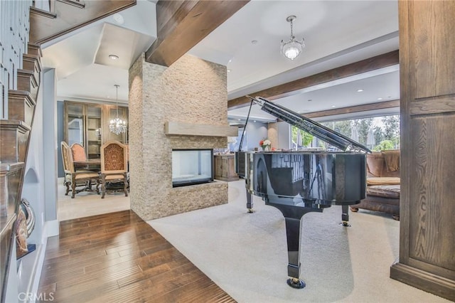 sitting room with beam ceiling, a notable chandelier, a multi sided fireplace, and wood finished floors