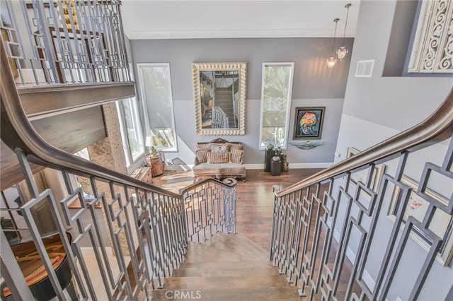 stairway with visible vents, baseboards, wood finished floors, and ornamental molding