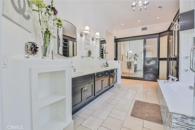 full bathroom with visible vents, a notable chandelier, a sink, tiled bath, and double vanity