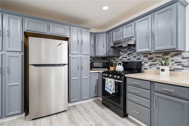 kitchen with gray cabinetry, light countertops, under cabinet range hood, appliances with stainless steel finishes, and tasteful backsplash