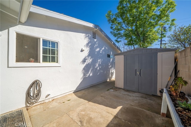 view of side of home with a shed, stucco siding, a patio, and an outdoor structure