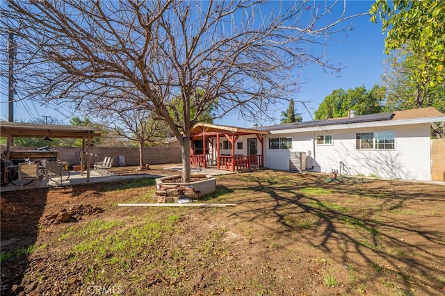 rear view of house featuring fence, a wooden deck, roof mounted solar panels, stucco siding, and a patio area