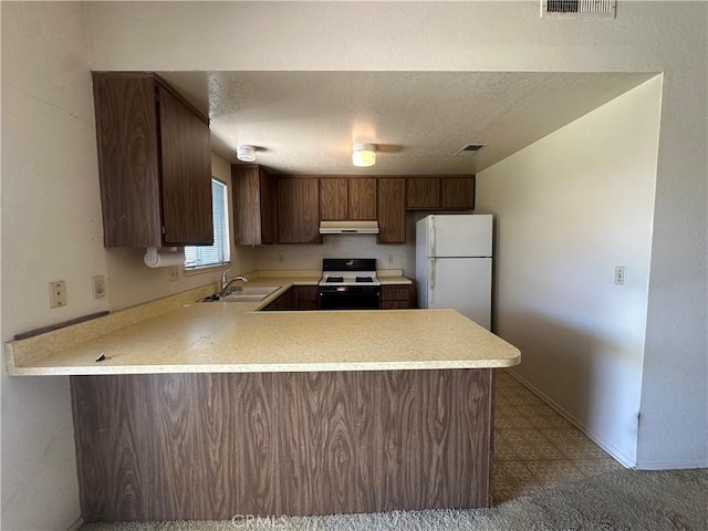 kitchen with range with gas stovetop, a peninsula, freestanding refrigerator, a sink, and under cabinet range hood