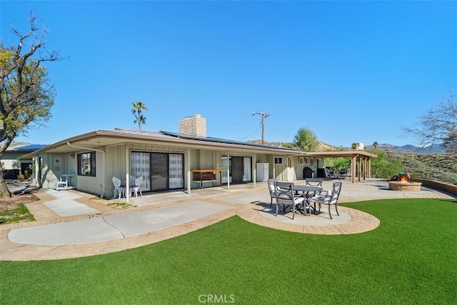 back of property featuring a yard, an outdoor fire pit, a patio area, solar panels, and a chimney