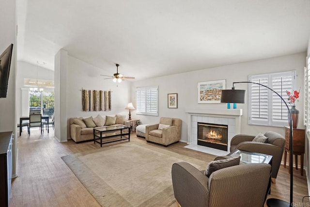 living area with a tiled fireplace, wood finished floors, a healthy amount of sunlight, and lofted ceiling