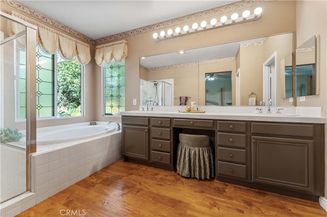 full bath featuring double vanity, a stall shower, wood finished floors, a bath, and a sink