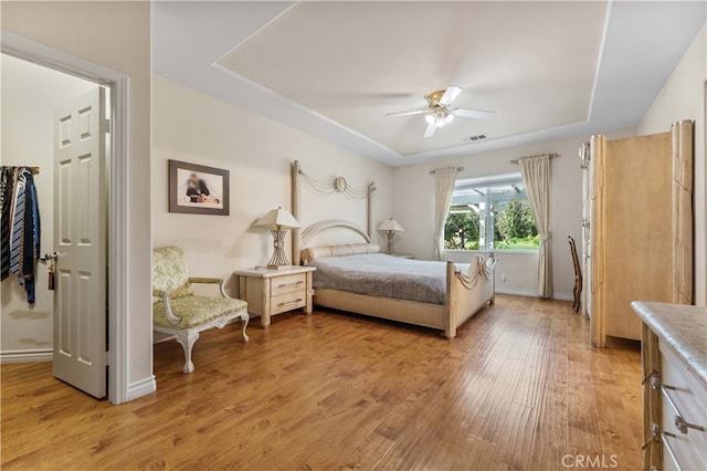 bedroom with visible vents, baseboards, light wood finished floors, a raised ceiling, and ceiling fan