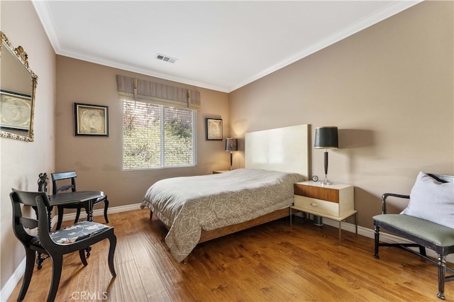 bedroom with visible vents, crown molding, baseboards, and wood finished floors