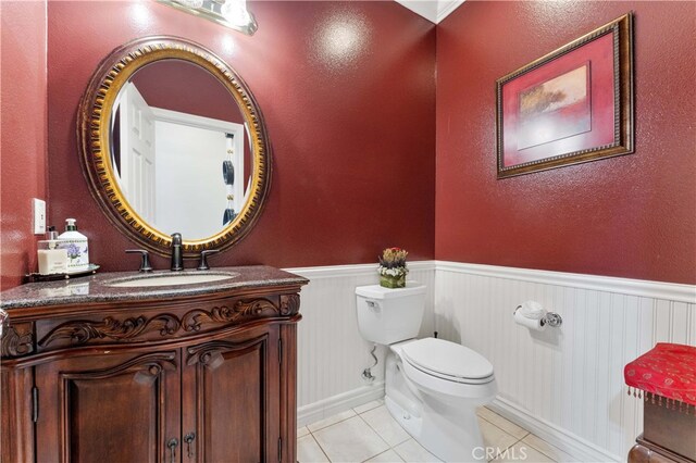 bathroom with tile patterned flooring, a wainscoted wall, toilet, and vanity