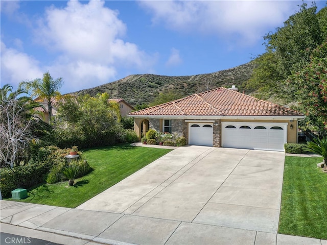 mediterranean / spanish-style home featuring stucco siding, stone siding, a mountain view, a front yard, and a tiled roof