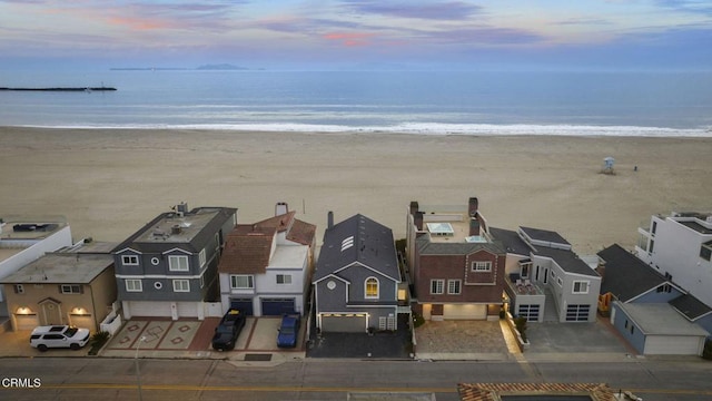 aerial view at dusk with a water view, a beach view, and a residential view