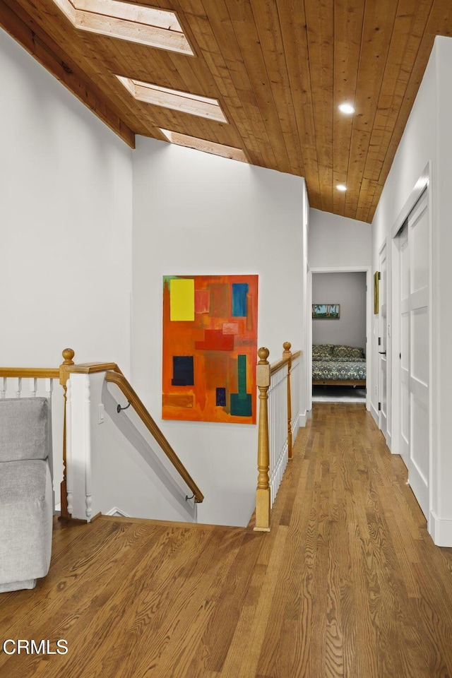 corridor featuring wood finished floors, recessed lighting, lofted ceiling with skylight, wooden ceiling, and an upstairs landing