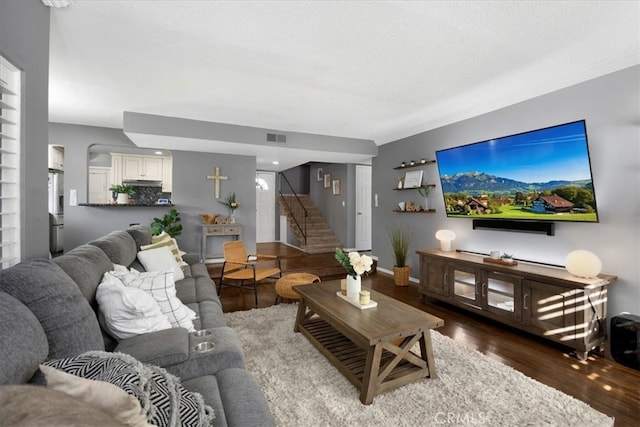 living area with stairway, wood finished floors, visible vents, baseboards, and crown molding