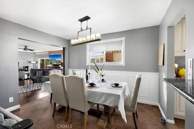 dining space featuring a textured ceiling, a healthy amount of sunlight, wainscoting, and a decorative wall