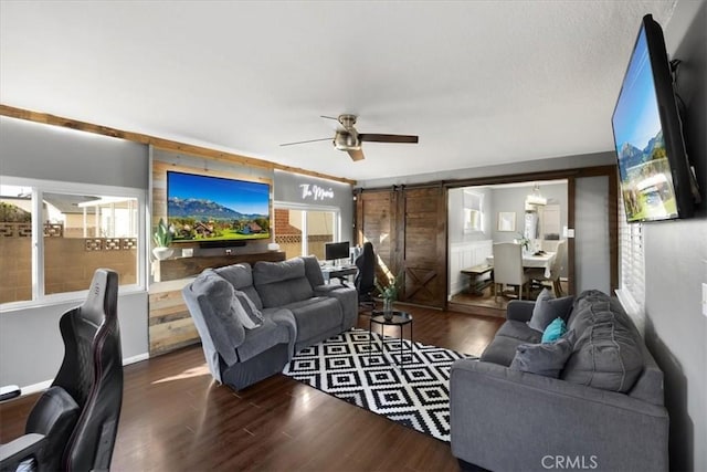 living area with a barn door, wood finished floors, baseboards, and ceiling fan