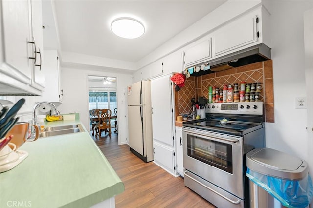 kitchen featuring a sink, backsplash, freestanding refrigerator, stainless steel range with electric cooktop, and light wood finished floors