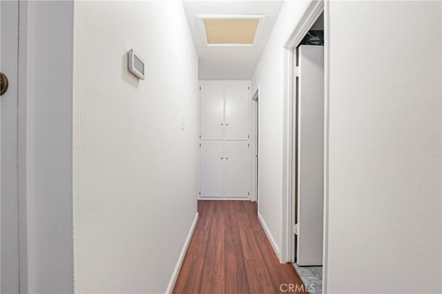 corridor with attic access, dark wood-type flooring, and baseboards