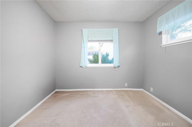 empty room with carpet flooring, a healthy amount of sunlight, a textured ceiling, and baseboards