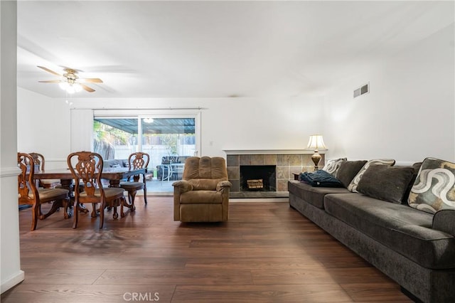 living area featuring a tiled fireplace, visible vents, ceiling fan, and dark wood-style flooring