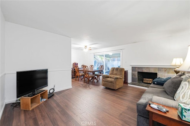 living room with a tiled fireplace, wood finished floors, baseboards, and a ceiling fan