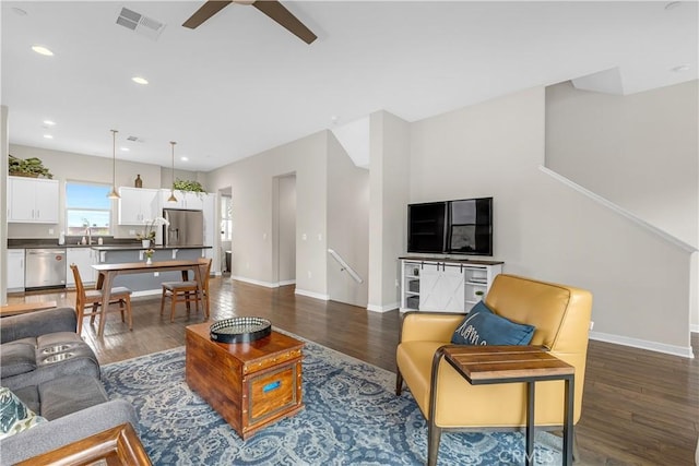 living area with dark wood finished floors, visible vents, baseboards, and ceiling fan