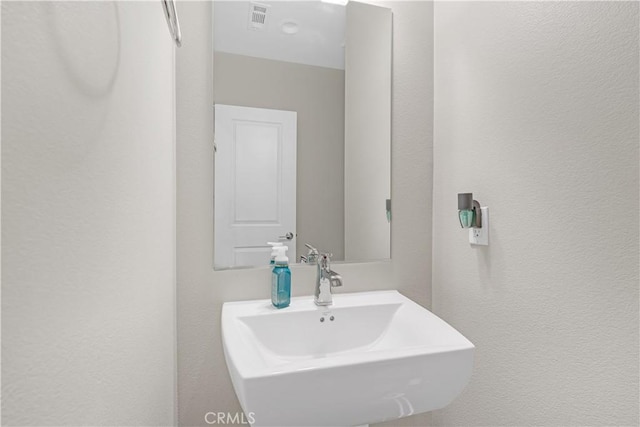 bathroom with a textured wall, visible vents, and a sink