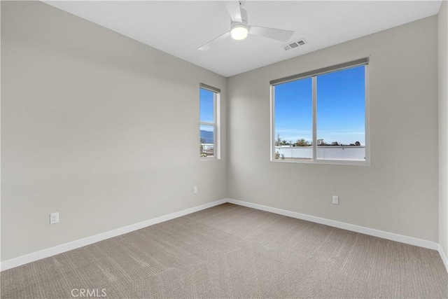 carpeted empty room featuring visible vents, a ceiling fan, and baseboards