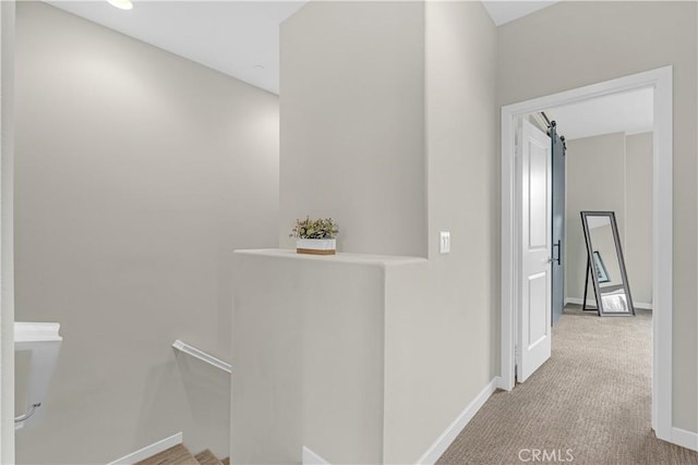 hall featuring an upstairs landing, a barn door, baseboards, and carpet floors