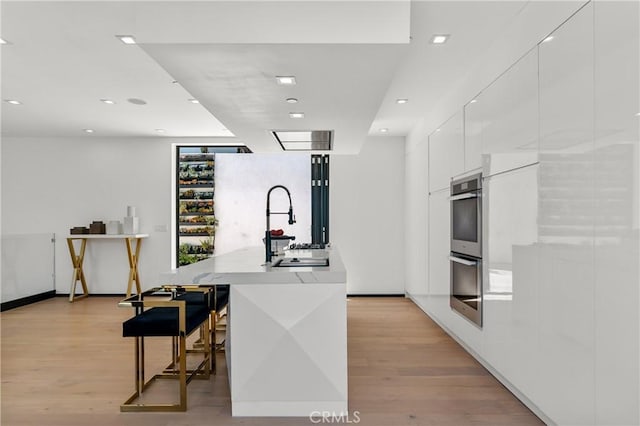 kitchen with a kitchen bar, light wood-style floors, modern cabinets, and white cabinetry