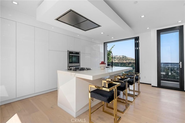 kitchen with modern cabinets, a center island with sink, white cabinetry, light wood-style floors, and stainless steel oven