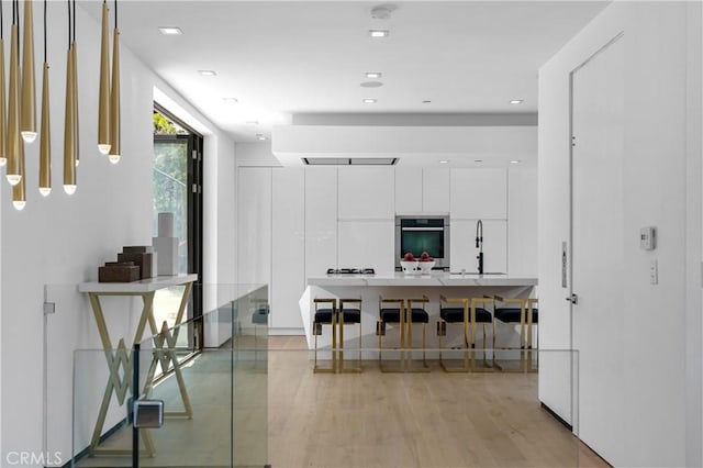 kitchen featuring stainless steel oven, light wood-style flooring, white cabinets, modern cabinets, and a sink