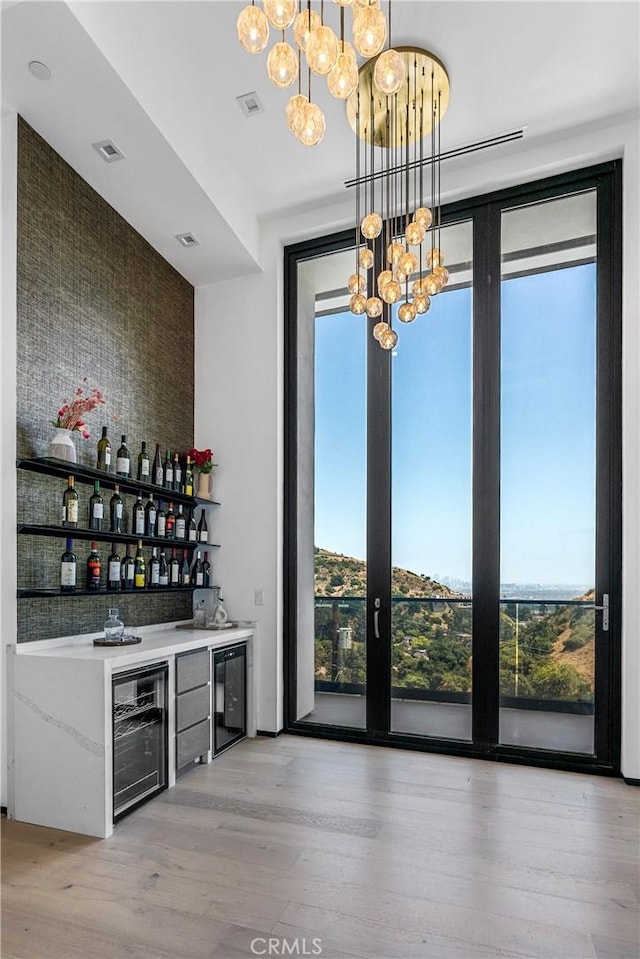 bar with hanging light fixtures, wine cooler, wood finished floors, and a dry bar