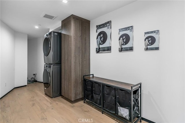 washroom with light wood-type flooring, visible vents, stacked washer / drying machine, baseboards, and laundry area