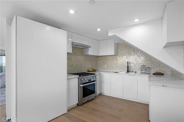 kitchen with under cabinet range hood, high end stainless steel range oven, a sink, white cabinets, and light countertops