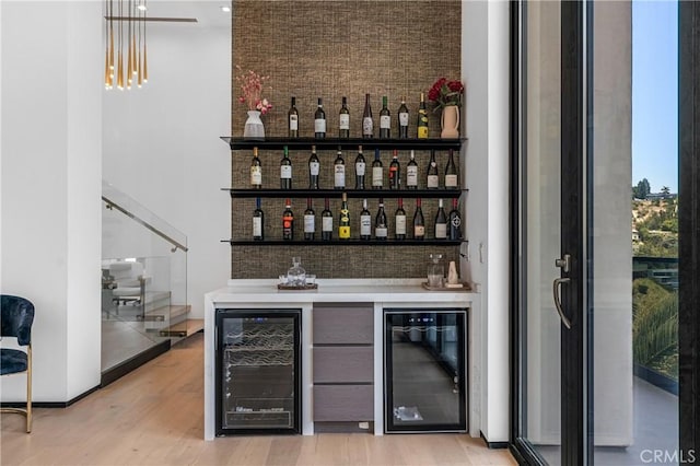 bar featuring light wood-style floors, wine cooler, a bar, and stairway