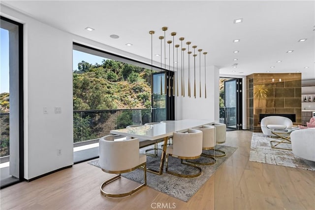 dining area featuring recessed lighting, a tiled fireplace, floor to ceiling windows, and light wood finished floors