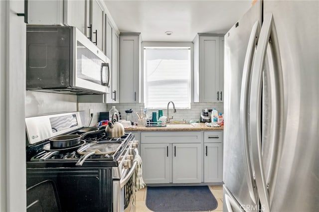 kitchen featuring backsplash, gray cabinets, appliances with stainless steel finishes, and a sink