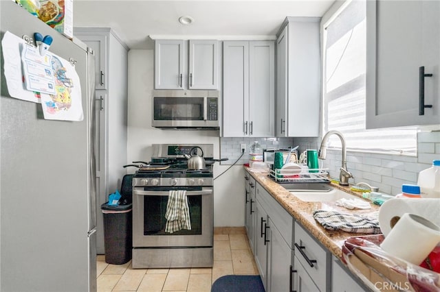 kitchen featuring gray cabinetry, a sink, backsplash, stainless steel appliances, and light tile patterned floors