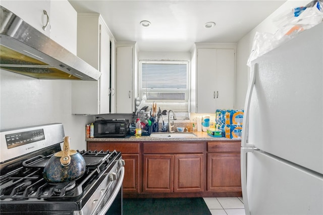 kitchen featuring stainless steel gas range oven, under cabinet range hood, freestanding refrigerator, light tile patterned flooring, and a sink